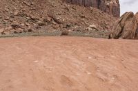 a person riding on an orange motorcycle across a dirt field with mountains in the background