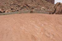 a person riding on an orange motorcycle across a dirt field with mountains in the background