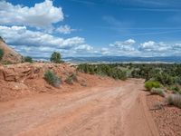 dirt road on an open, rocky terrain area with mountains in the background and clouds overhead