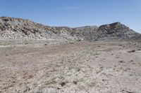 large area covered in scruby land with tall mountain behind it and dirt area with no grass