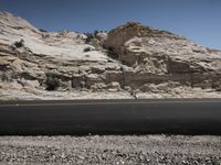 the black paved road is next to a large rocky area that contains a rock and a small cactus