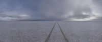 a very wide open plain with tracks leading to the horizon and dark clouds in the distance