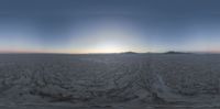 a fish eye view of an empty plain near mountains at sunset with the sun shining