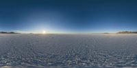 the sun shines over the horizon on a snowy field with tracks and footprints of people