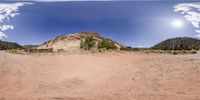 a 360 - lens view of a mountain with some hills in the background, and a dirt area beneath it