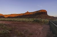 a stop sign is by a red desert with cliffs in the background and grass below it