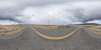 a winding road on a cloudy day with mountains in the distance and a single lane yellow strip