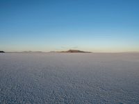 a snow covered area with a small mountain in the distance, and a clear blue sky above