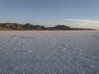 a man walking on the snow with no shoes and mountains in the background in the distance