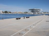 an empty concrete pier with water and buildings in the background are nearby the seafront
