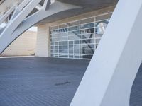 large white architectural structure in front of glass door that reads open, and next to sidewalk area with plants