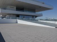 a curved building that is white in color on top of a brick walk way between the building and stairs