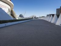 a walkway surrounded by concrete cone poles near a museum and buildings near the sea side
