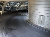 a long, curved walkway with concrete walls on either side of it is empty and the train is coming up