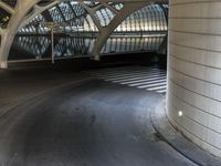 a long, curved walkway with concrete walls on either side of it is empty and the train is coming up