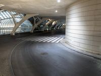 a long, curved walkway with concrete walls on either side of it is empty and the train is coming up