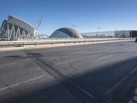 a road by a bridge and building under a blue sky with white lines on the sidewalk