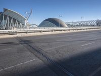 a road by a bridge and building under a blue sky with white lines on the sidewalk