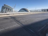 a road by a bridge and building under a blue sky with white lines on the sidewalk