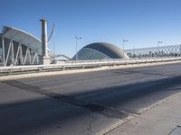 a road by a bridge and building under a blue sky with white lines on the sidewalk