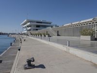 the sidewalk is empty in the foreground of the building and a boat dock at right