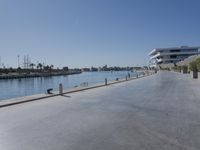 an empty walkway beside a waterway with several parked boats on it and a glass building behind