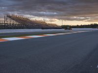 a man racing a race car down a race track at dusk with other people watching