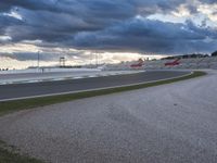 a road with racing cars at dusk with a cloudy sky over it and the camera and lights of several cars visible