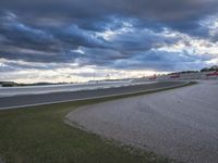 a road with racing cars at dusk with a cloudy sky over it and the camera and lights of several cars visible