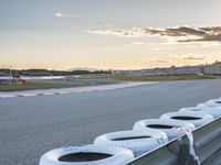 a group of tires sit on the edge of a track at sunset near an airport