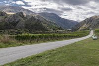 a van driving through the countryside by a vineyard, near mountains and trees that look out across the land