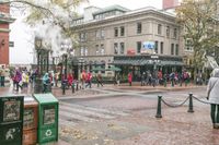 people standing on a street in a city while steam comes from them pipes to the building