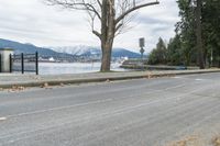 a paved road next to the edge of a lake with a snow - capped mountain