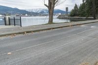 a paved road next to the edge of a lake with a snow - capped mountain