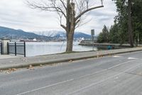 a paved road next to the edge of a lake with a snow - capped mountain