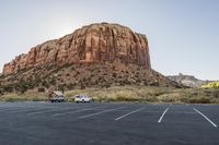 two vans parked in the middle of a parking lot near rocks and a mountain in the background