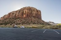 two vans parked in the middle of a parking lot near rocks and a mountain in the background