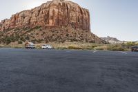 two vans parked in the middle of a parking lot near rocks and a mountain in the background