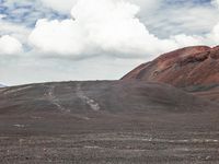 a large open dirt area with some red hills and clouds in the distance, and a person on a horse standing at the end of the path