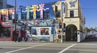 the corner is covered in a variety of murals, including a man walking next to a building with colorful mural