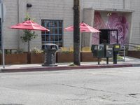 there are several umbrellas on this street corner, along with a traffic light on a pole