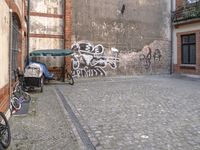 bicycles parked in front of an old building with graffiti on the side of it and a brick wall and street with a sign