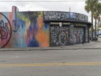 a building with graffiti is sitting next to a street with parked cars and palm trees