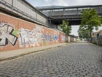 a brick wall with graffiti on it in an empty street, underpass bridge and overhead walkway