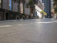 the empty road is next to a city sidewalk and many buildings with trees on both sides