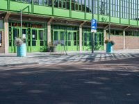 a green building with a street sign and blue containers on the side of it in front of it