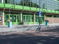 a green building with a street sign and blue containers on the side of it in front of it