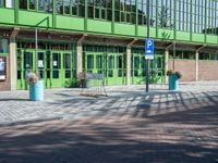 a green building with a street sign and blue containers on the side of it in front of it