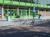 a green building with a street sign and blue containers on the side of it in front of it