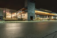 an outside restaurant lit up with a clock on the front of it in the dark